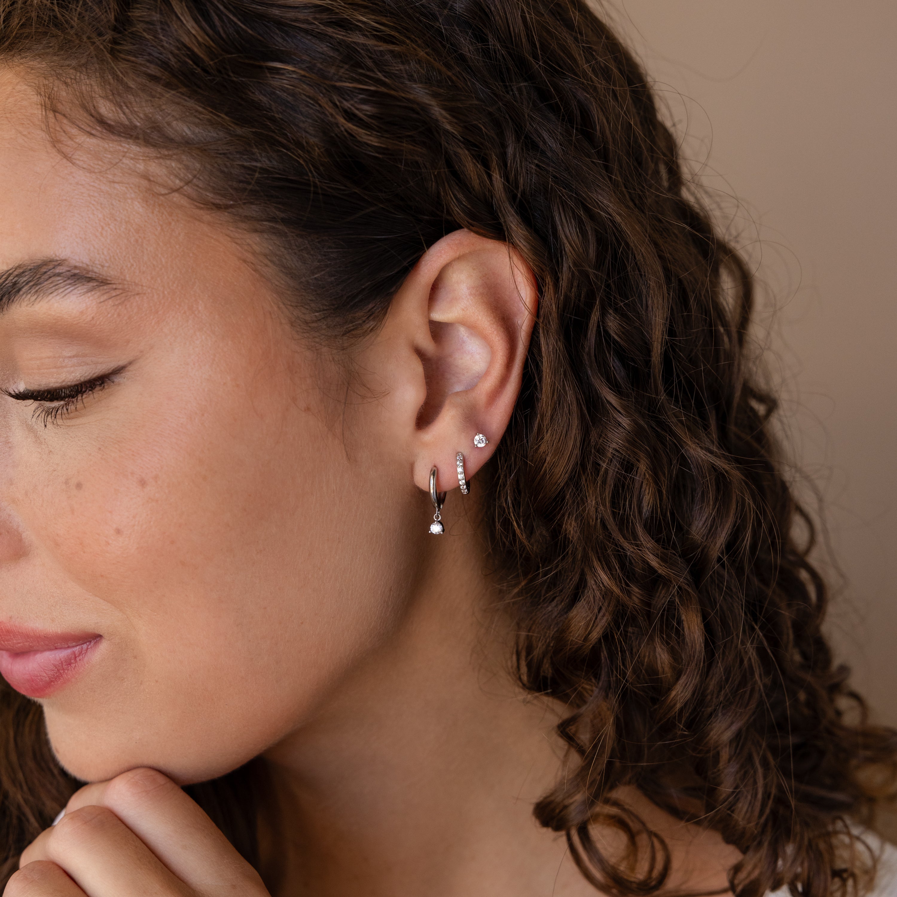 A woman with curly hair smiles gently while wearing the Classic Diamond Earrings Set in Sterling Silver.