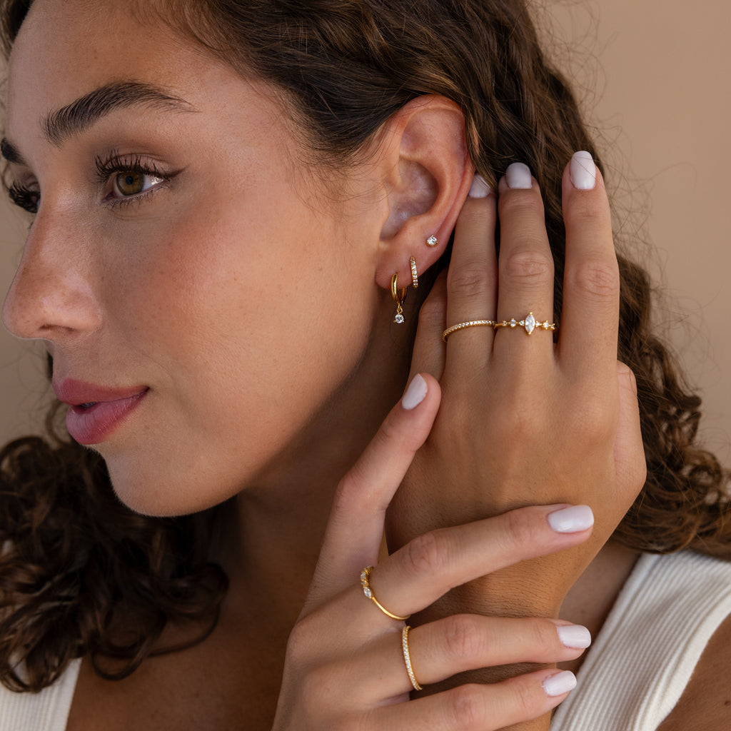 Woman with curly hair wearing a white top and gold rings, showcasing the Classic Diamond Earrings Set as her elegant wedding jewelry.