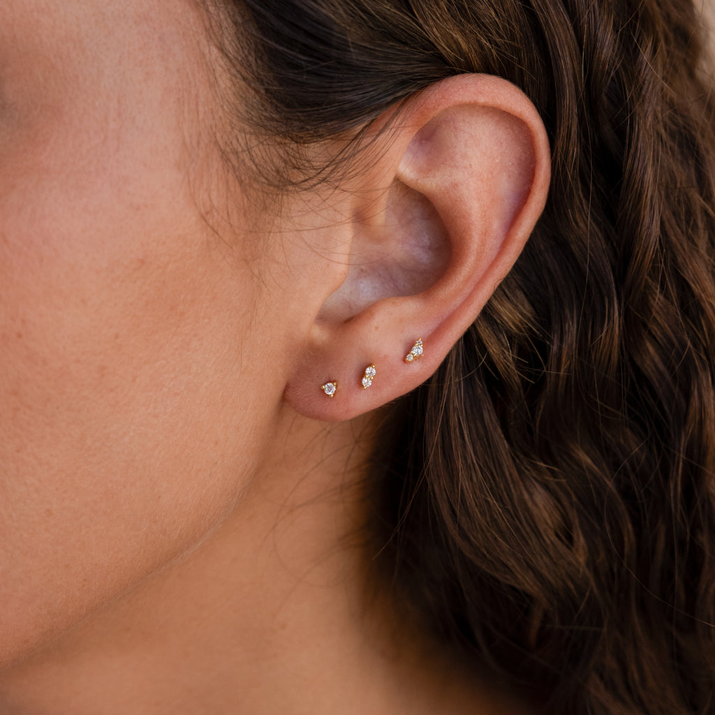 Close-up of a woman's ear wearing the Tiny Diamond Flatback Studs Set—three small gold diamond studs in a row on the earlobe, offering elegant style and comfortable wear.