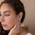 A woman with wavy hair touches her ear, showing off three Tiny Diamond Flatback Studs Set in Sterling Silver, paired with natural makeup.