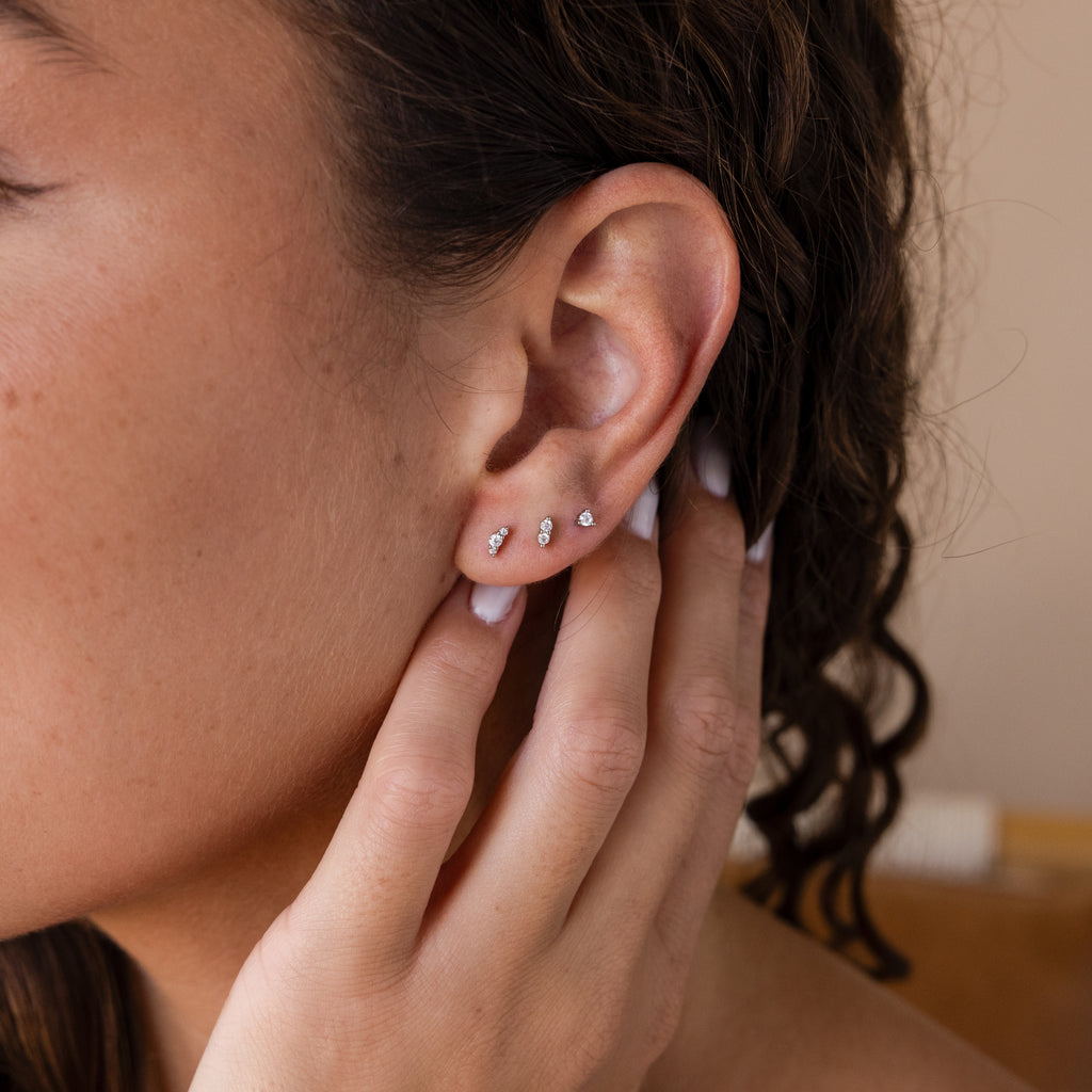Close-up of a person wearing the Tiny Diamond Flatback Studs Set—three delicate diamond studs in their ear—gently touching their ear with their hand.
