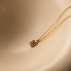 North Star Birthstone Necklace in Amethyst (February) featuring a rectangular purple crystal pendant on a gold chain, displayed on a smooth beige background.