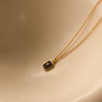 The North Star Birthstone Necklace in sapphire for September features a rectangular dark crystal pendant with a diamond-set North Star, displayed on a smooth beige surface.