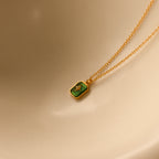 North Star Birthstone Necklace in Emerald (May) with a rectangular crystal pendant, displayed on a beige curved surface.
