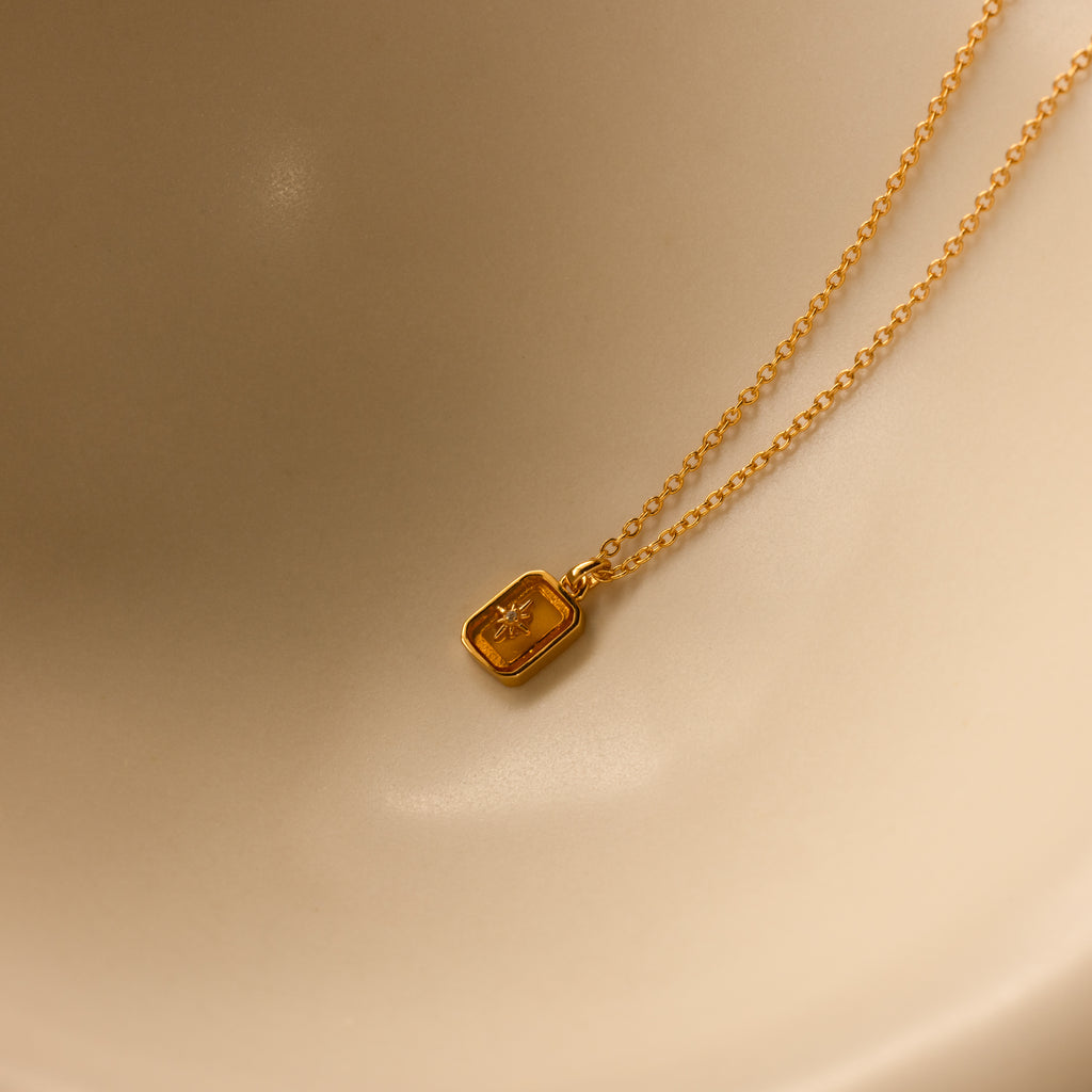 A North Star Topaz Necklace with a star engraving is displayed on a smooth, light beige surface.