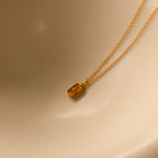 A North Star Topaz Necklace with a star engraving is displayed on a smooth, light beige surface.