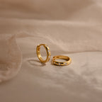Two Mini Diamond Sprinkle Huggies with sparkling diamonds are shown on soft beige fabric under gentle lighting.