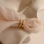 The Mini Diamond Sprinkle Huggies, two gold hoops adorned with sparkling diamonds, are displayed on a soft, light pink textured fabric.