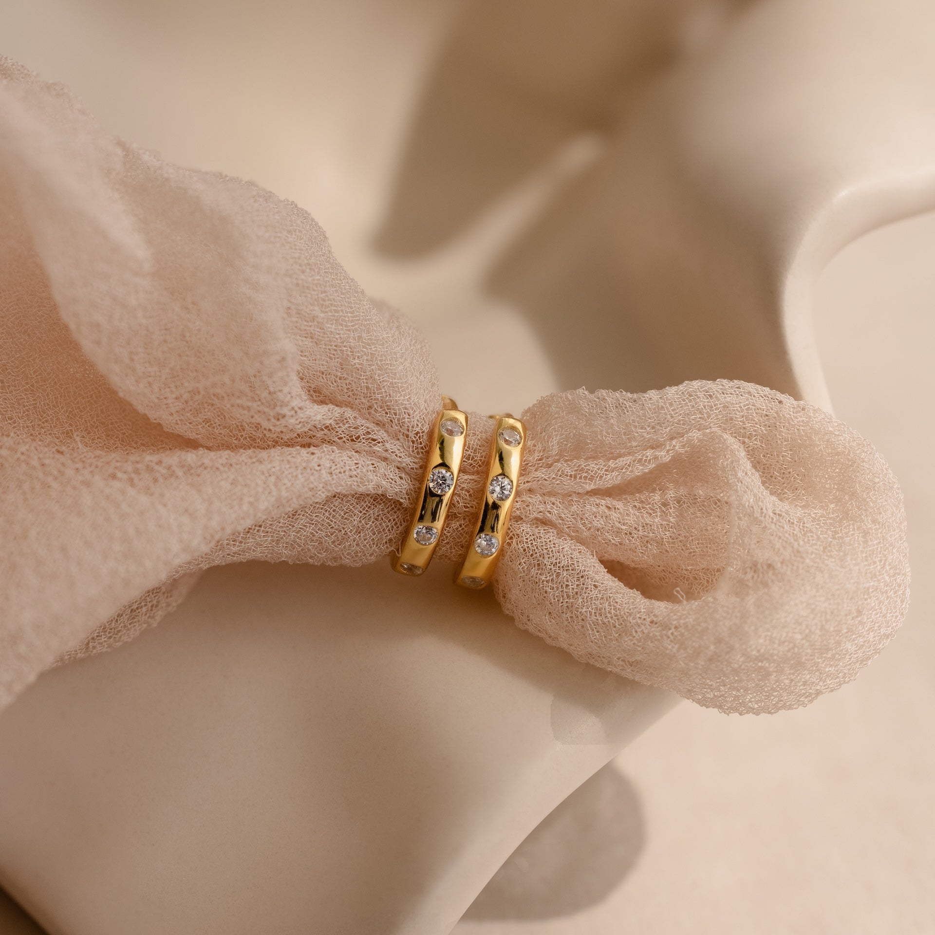 The Mini Diamond Sprinkle Huggies, two gold hoops adorned with sparkling diamonds, are displayed on a soft, light pink textured fabric.