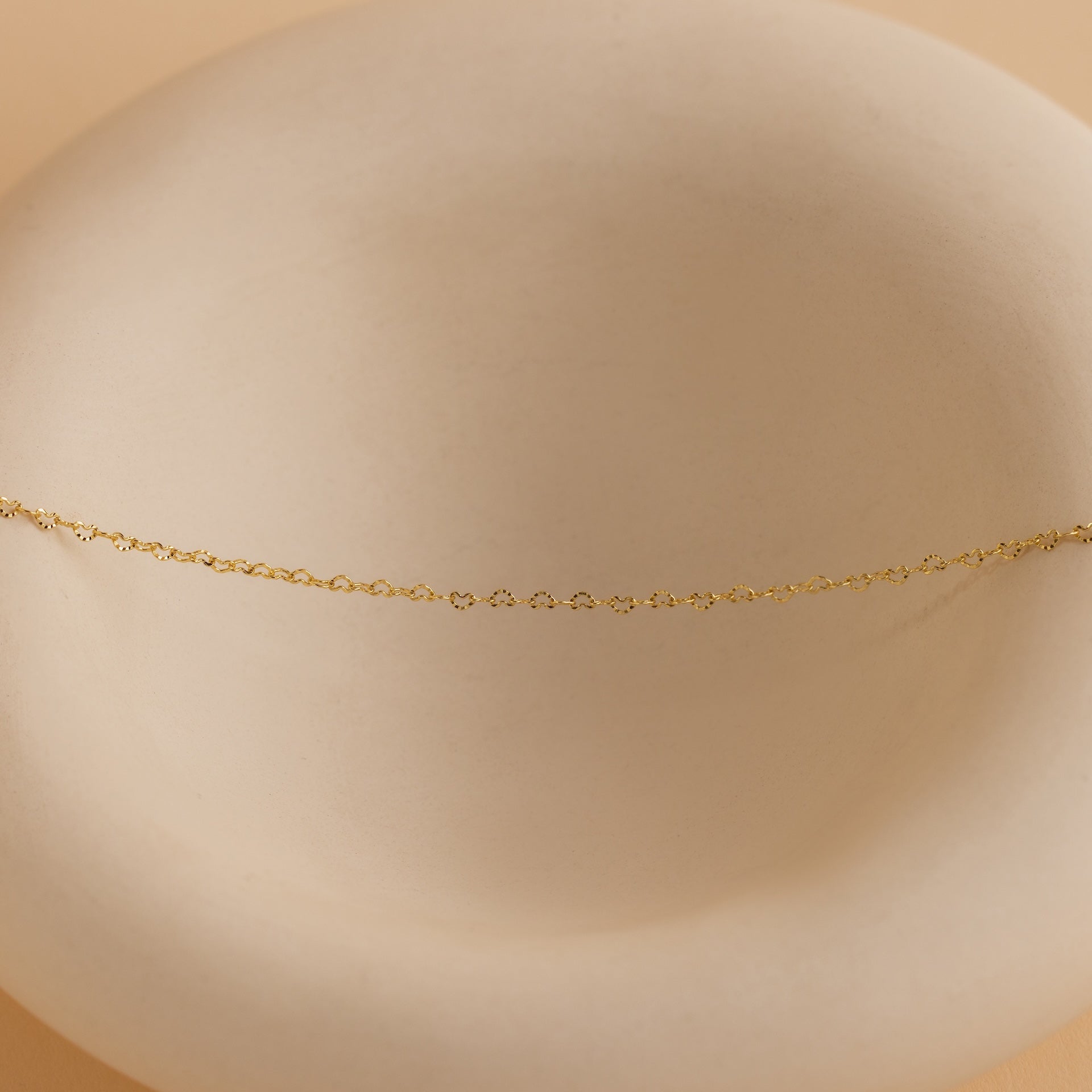 Heart Link Chain Necklace in 18K Gold displayed on a smooth, round, off-white dish with a soft beige background.