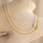The Nella Pave Off-Center Initial Necklace, featuring a delicate chain and personalized initial pendant, is displayed on a beige stand. Layer it for a chic look with gold or silver necklaces.