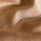 A delicate white gold double chain forms a loose knot on soft, light brown fabric—a perfect Love Knot Bracelet in White Gold gift for couples.