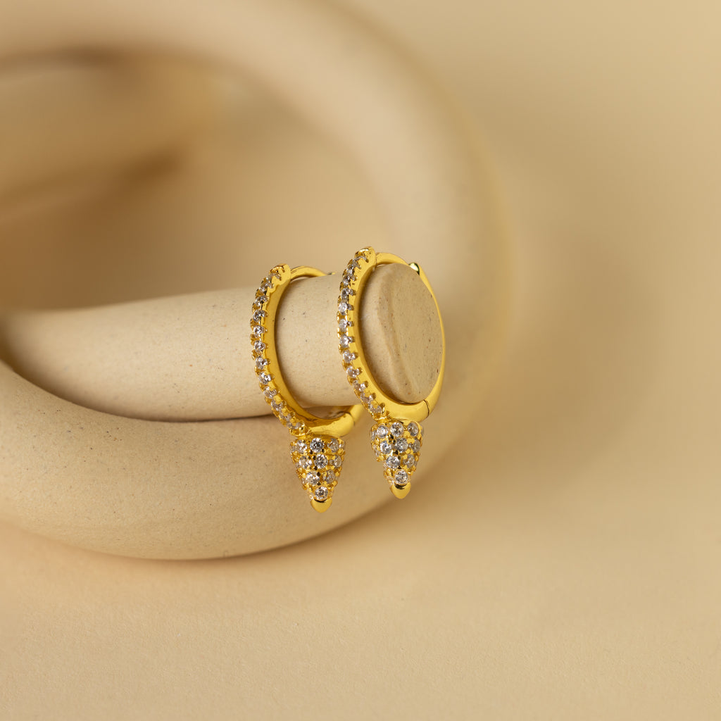 Pave Spike Huggies featuring diamond accents and a bold cone design, displayed on a beige curved surface.