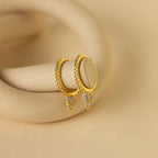 Pave Spike Huggies featuring diamond accents and a bold cone design, displayed on a beige curved surface.