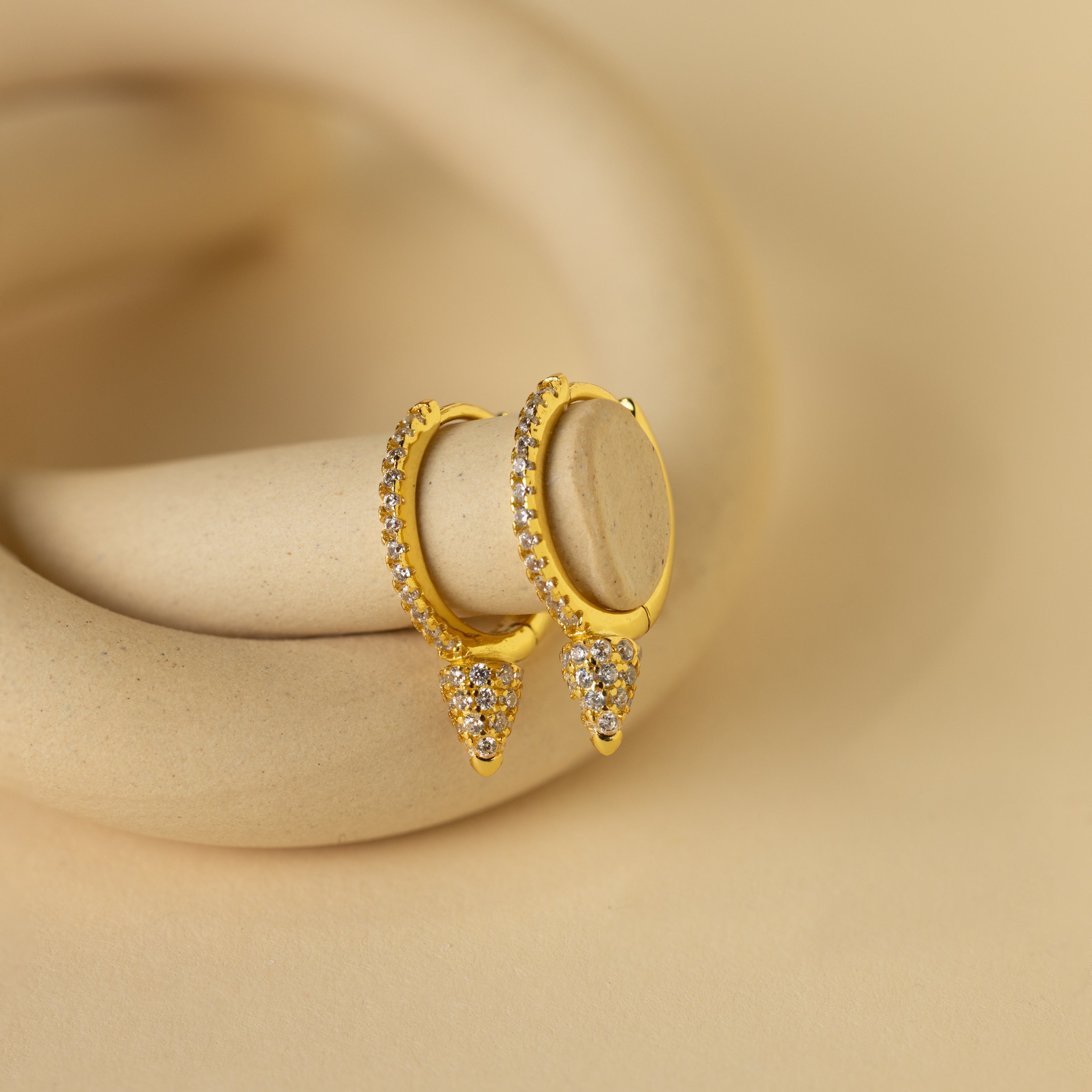 Pave Spike Huggies featuring diamond accents and a bold cone design, displayed on a beige curved surface.