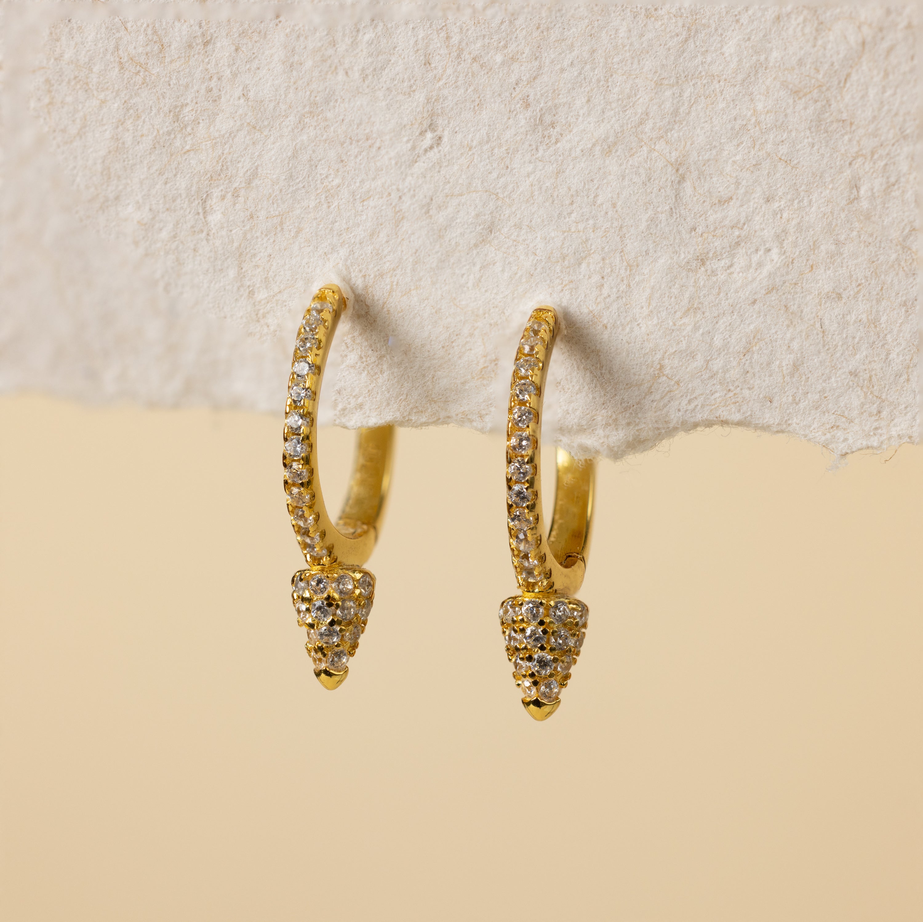 Pave Spike Huggies with diamond accents displayed on a textured off-white surface against a beige background.