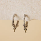 Minimalist jewelry: Pave Triple Spike Huggies—silver hoop earrings with small clear stones and pointed tips, shown on textured off-white paper.