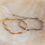 The Triple Snake Chain Bracelet, shown in both gold and silver on a beige marble surface, is ideal for layering and suits those who love minimal jewelry.
