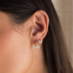 Close-up of a womans ear wearing two gold earrings: Diamond Bow Huggies and a dainty flower stud.