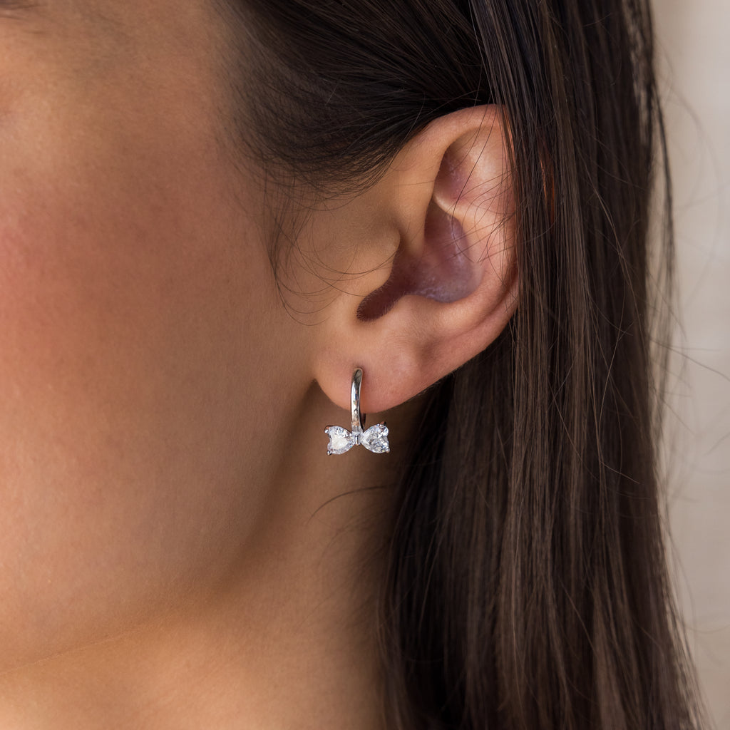 A close-up of a womans ear wearing Diamond Bow Huggies in Silver, styled with dainty diamond earrings for an elegant look.