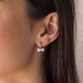 A close-up of a womans ear wearing Diamond Bow Huggies in Silver, styled with dainty diamond earrings for an elegant look.