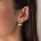 A close-up of a womans ear wearing Diamond Bow Huggies in Silver, styled with dainty diamond earrings for an elegant look.