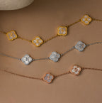 Three Pearl Clover Letter Necklaces, each with clover-shaped charms and the letters L E A H, R B S, and T D, are displayed on a brown background, showcasing their personalized elegance.