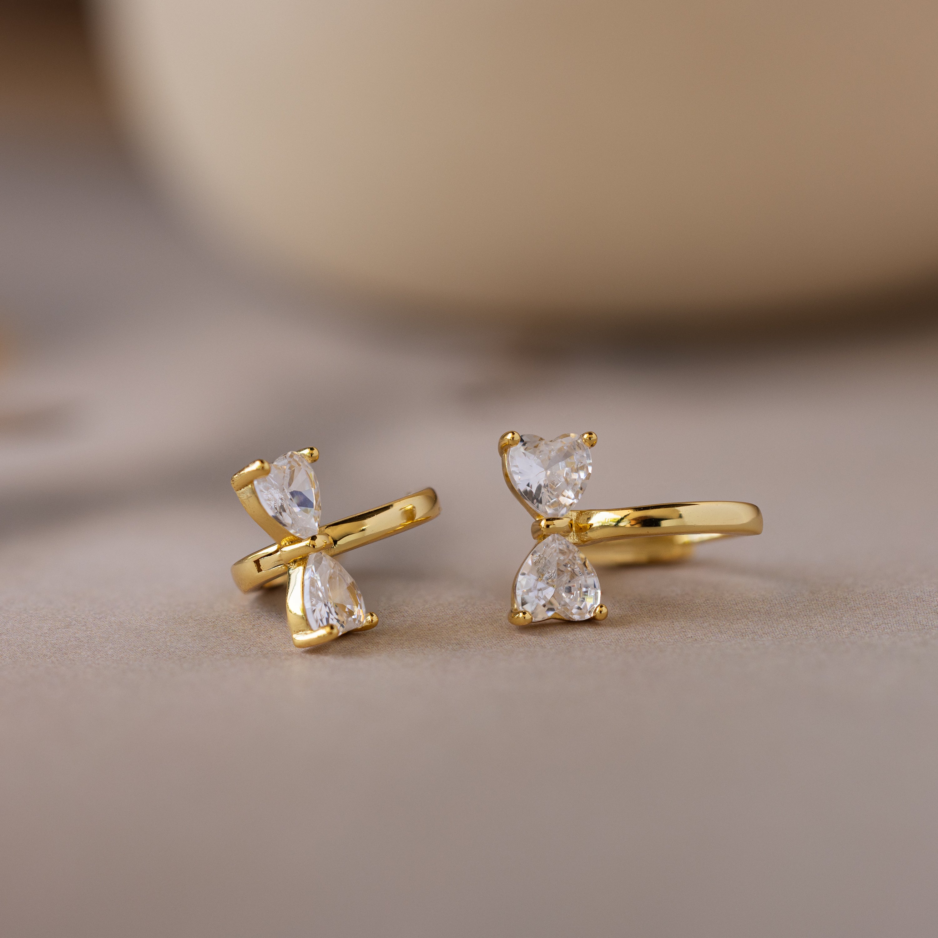 Diamond Bow Huggies featuring two vertically set pear-cut clear gemstones, displayed on a soft beige surface.