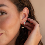 Close-up of a woman’s ear wearing Ombre Opal Huggies, a star dangle earring, and a small crescent moon earring.