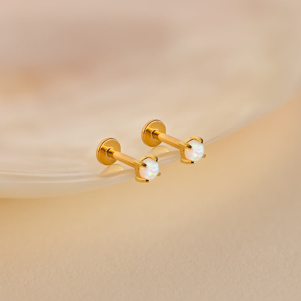 The Opal Flat Back Studs feature round opal gemstones set in gold, displayed on a soft beige surface.