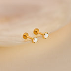 The Opal Flat Back Studs feature round opal gemstones set in gold, displayed on a soft beige surface.