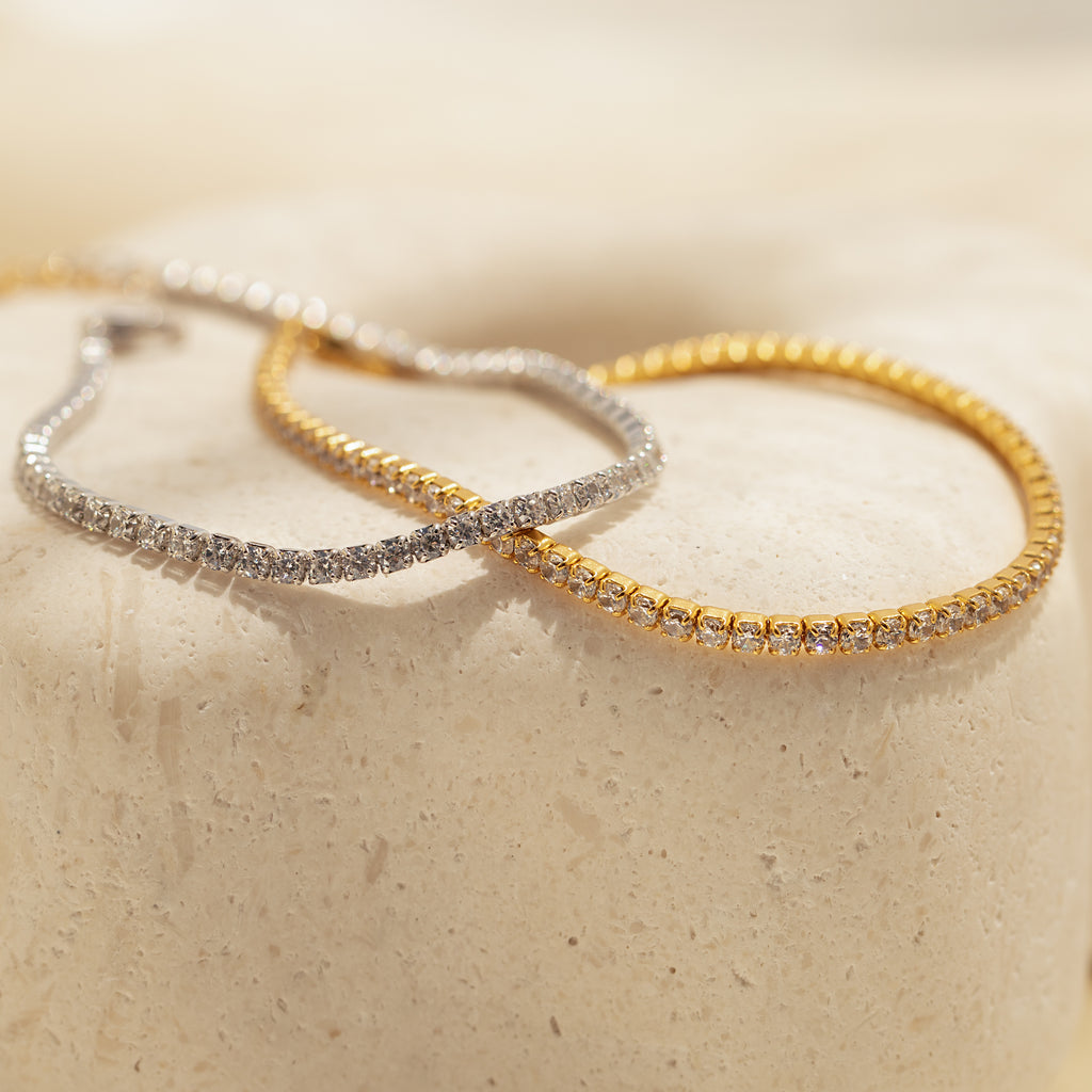 The Classic Diamond Tennis Bracelet in white gold with clear stones, displayed on a textured cream surface—a timeless addition to any elegant jewelry collection.
