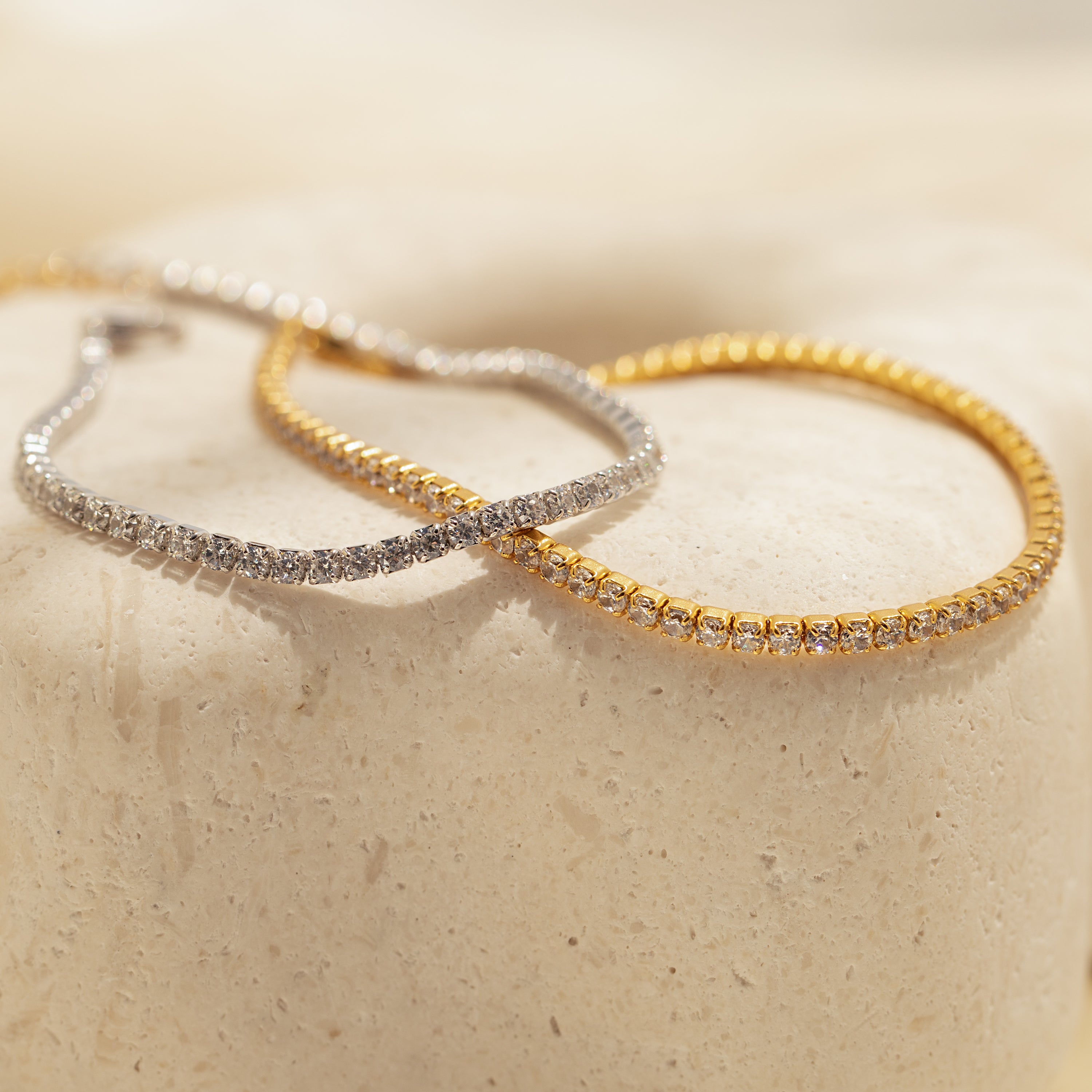 The Classic Diamond Tennis Bracelet in white gold with clear stones, displayed on a textured cream surface—a timeless addition to any elegant jewelry collection.