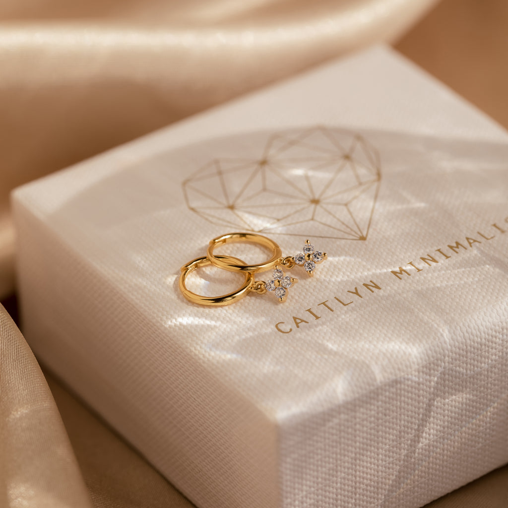 A pair of gold Diamond Flower Huggie earrings resting atop a textured cream-colored jewelry box