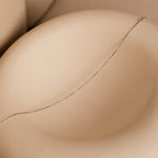 The Micro Rolo Chain Anklet in Sterling Silver is displayed on a smooth beige curved surface, its delicate silver chain highlighted by soft shadows.