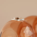 The Paris Thin Name Signet Ring in Sterling Silver, engraved with Sam, is displayed on a glossy peach surface.