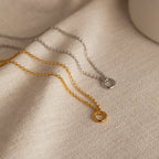 The Rolo Circle Charm Necklace, a minimalist gold or silver necklace with a small circular pendant, is elegantly displayed on light beige fabric.