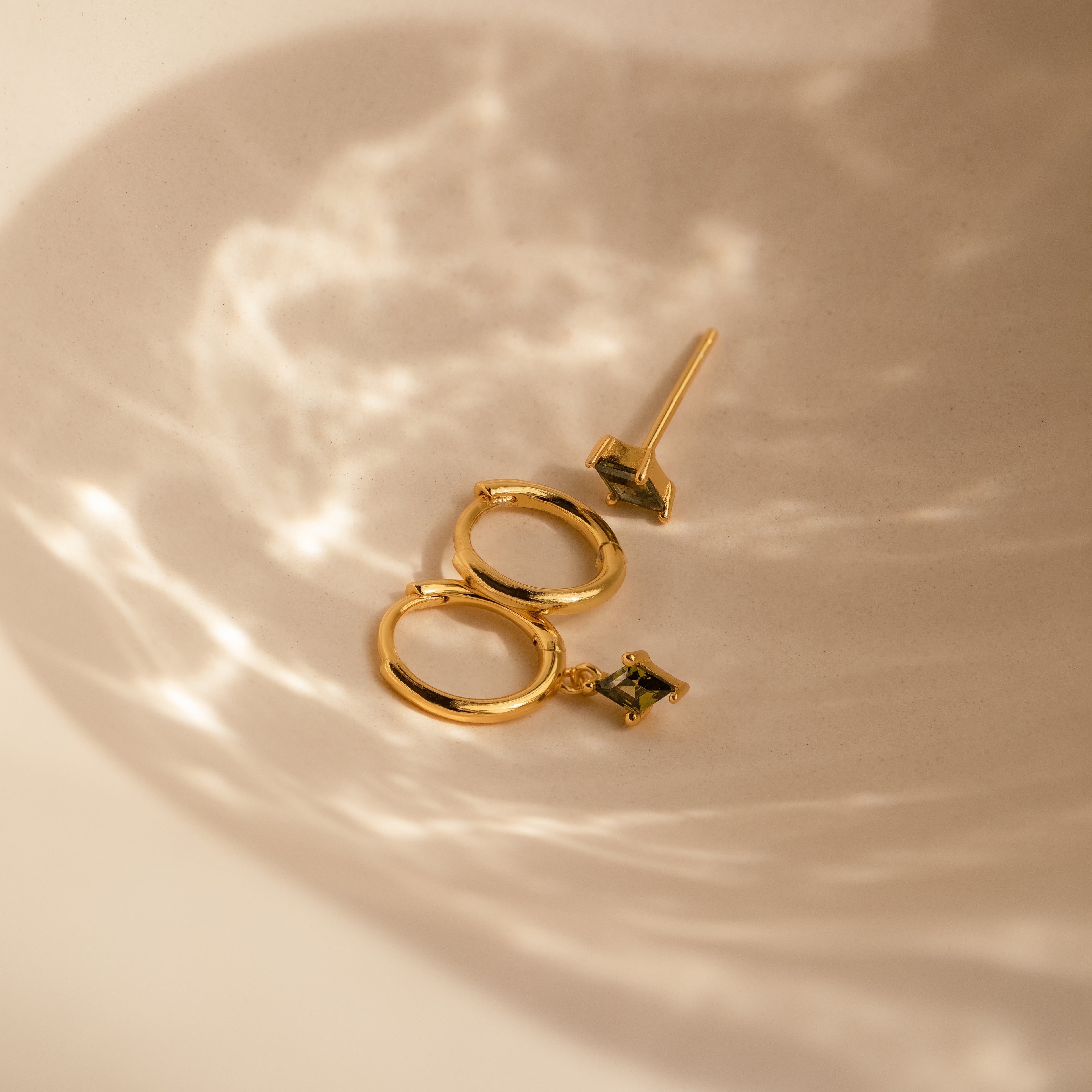 The Peridot Earrings Set in 18K Gold is displayed in a softly lit, neutral dish—ideal for stacking or as a chic cartilage earring.