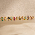 The Triple Pearl Huggies, along with other colorful gemstone and pearl stud earrings, are displayed on a textured beige surface.