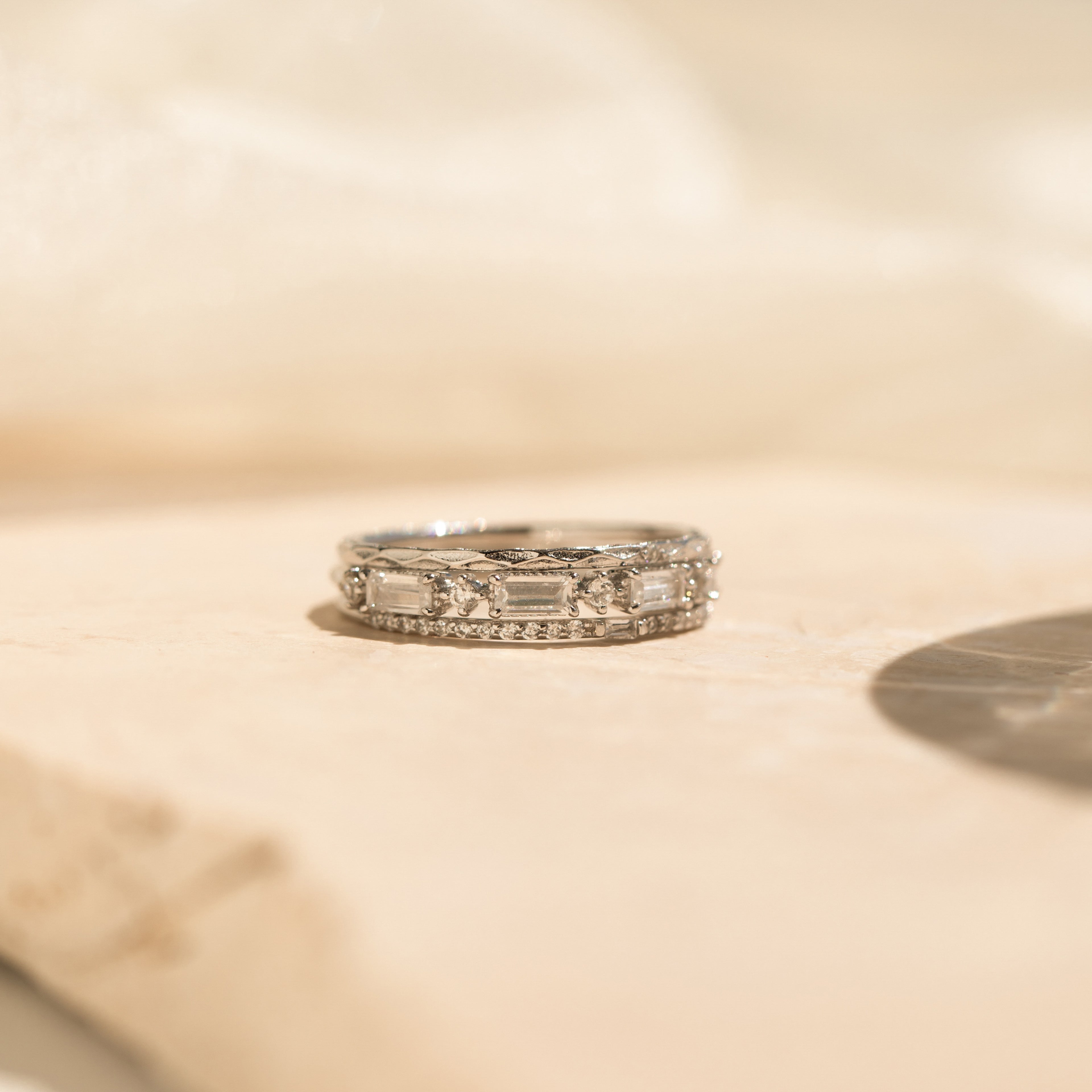 The Diamond Stacking Ring Set in Sterling Silver shines on a light beige stone surface in soft, natural light—a refined set ideal for stacking or gifting, especially as a thoughtful Christmas present.