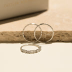 The Diamond Stacking Ring Set in Sterling Silver, featuring three delicate rings with a diamond accent, is beautifully displayed on a beige stone surface—an elegant choice for a Christmas gift.