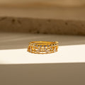 The Crystal Stacking Ring Set in 18K Gold features two rows of sparkling crystal gemstones, elegantly displayed on a sunlit surface with a neutral background—a stunning jewelry piece.