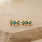 Triple Blue Zircon Huggies featuring three round blue zircon stones on a beige stone surface—perfect customizable gemstone earrings for minimalist hoop lovers.