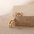 Triple Diamond Huggies gold earrings feature three sparkling diamonds each, displayed on a light beige stone surface—an ideal pick for minimalist jewelry lovers.