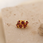 The Triple Garnet Huggies, gold rings featuring six red garnets, are displayed on a textured beige stone surface, blending minimalist hoop elegance with the personalized allure of customizable birthstone earrings.