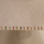 Twelve pairs of Aquamarine Drop Studs, perfect as birth month jewelry, are displayed in a row on a beige textured surface.