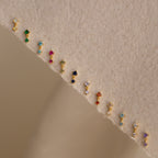 A row of sparkling Diamond Drop Studs is arranged on a textured beige surface, making each accessory a dazzling highlight for any jewelry collection.