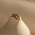 Topaz Drop Studs birthstone earrings with small crystals in gold and silver, a chic accessory, shown on a smooth cream ceramic vase.