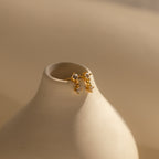Topaz Drop Studs birthstone earrings with small crystals in gold and silver, a chic accessory, shown on a smooth cream ceramic vase.