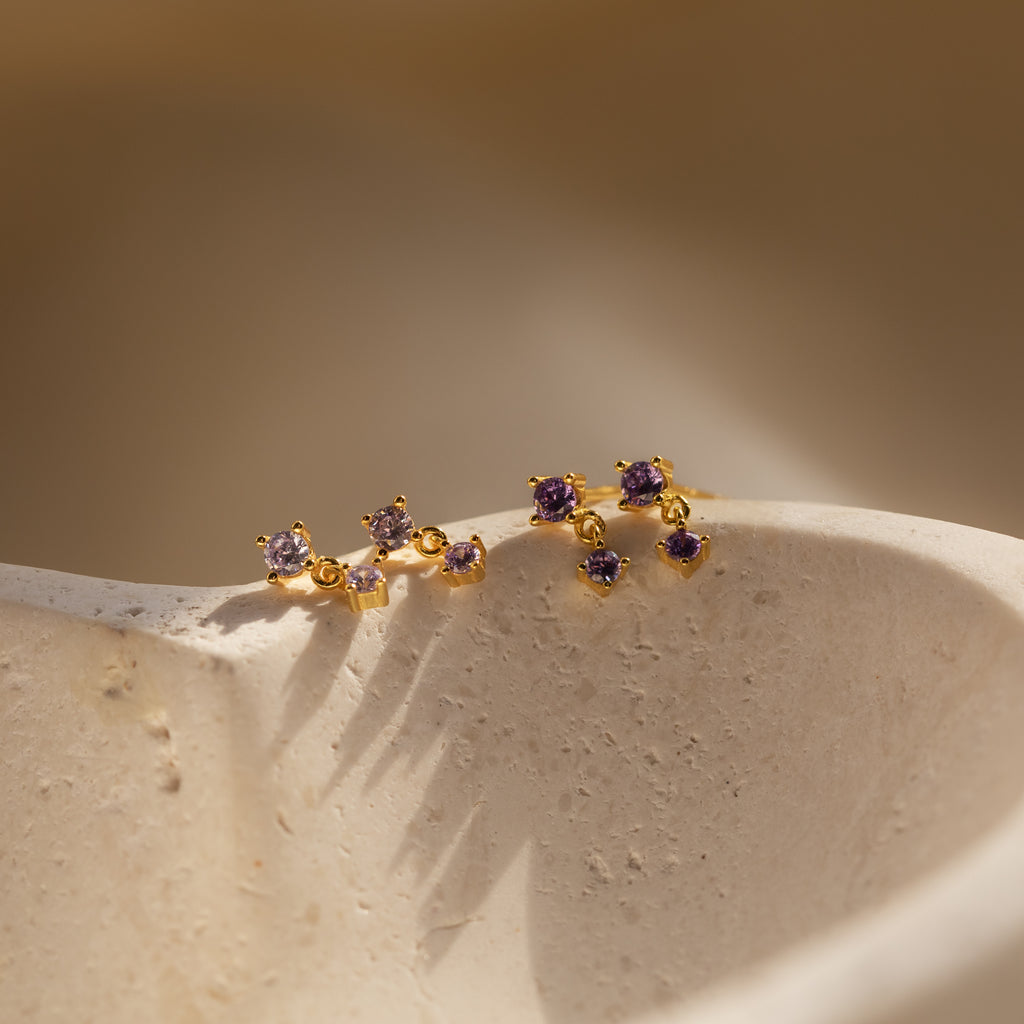Alexandrite Drop Studs featuring small purple gemstones, perfect as gemstone studs or birthstone drop studs, displayed on a textured off-white surface in soft light.